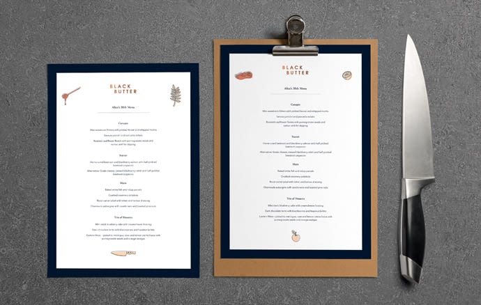 2 samples of Black Butter menus. One is on card and the other is on a clipboard. They are photographed from above on a concrete surface with a chef's knife to the right.