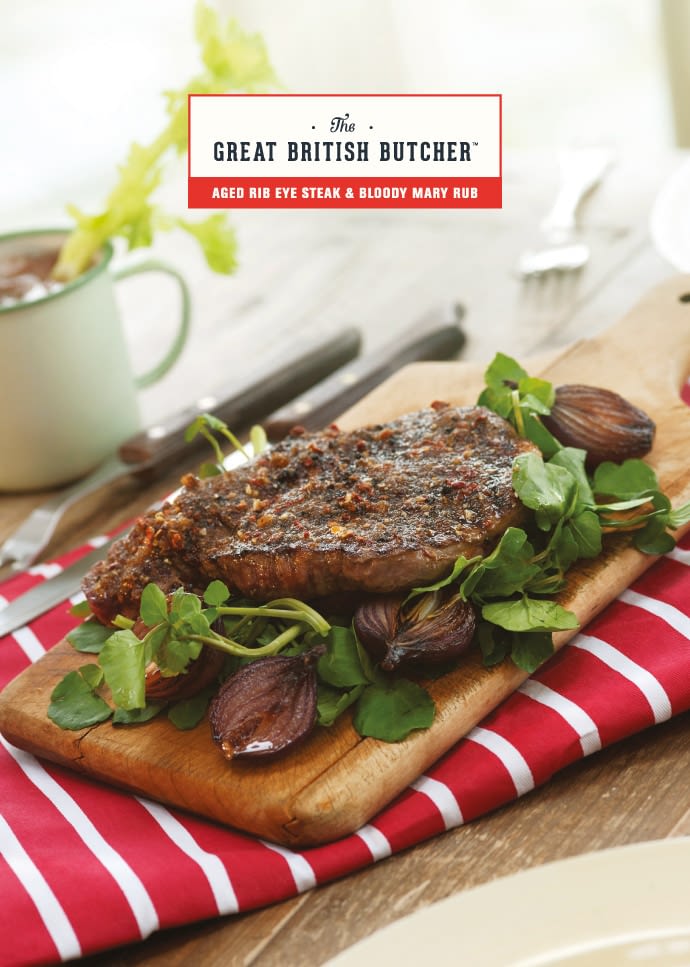 The front of a branded recipe card, presenting a rib eye steak on a small wooden serving board, with watercress and onions - prepared with Bloody Mary Rub. The board is situated on top of a red and white striped folded apron, next to a traditional enamel cup filled with a Bloody Mary and topped with a celery stalk.
